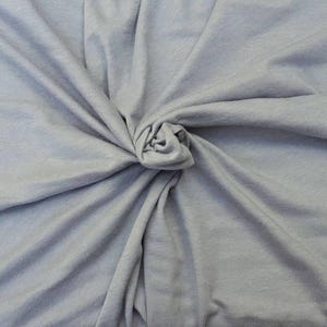 Puede incluir: Una tela de color gris claro con una textura suave y mate, recogida en el centro para crear pliegues y drapeados naturales que irradian hacia afuera. El material muestra un color s&oacute;lido y consistente, resaltando el tejido fino del textil.