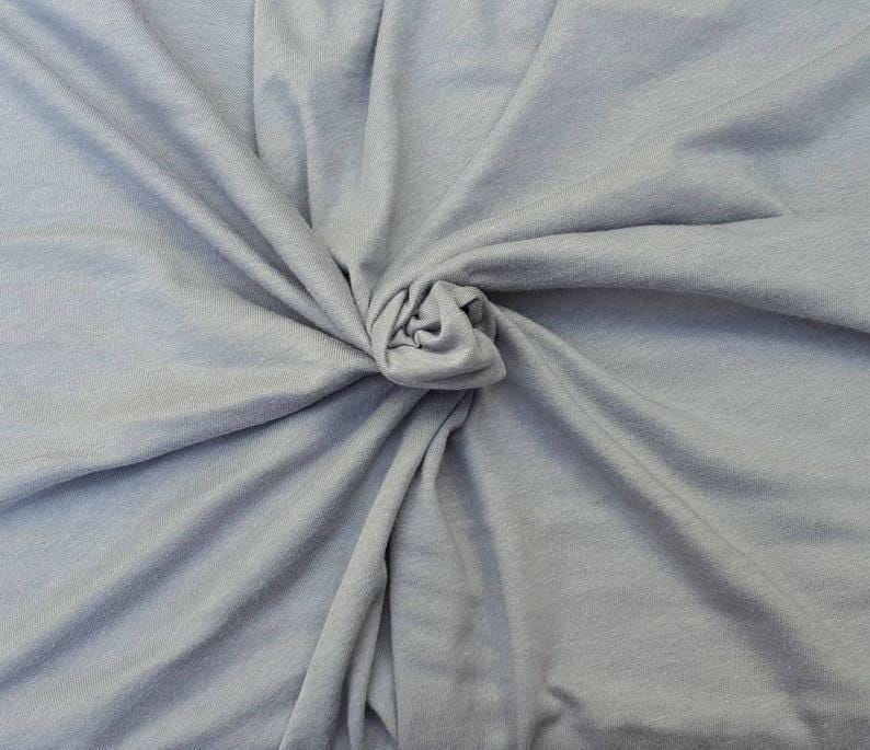 Puede incluir: Una tela de color gris claro con una textura suave y mate, recogida en el centro para crear pliegues y drapeados naturales que irradian hacia afuera. El material muestra un color s&oacute;lido y consistente, resaltando el tejido fino del textil.