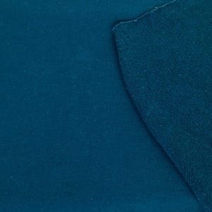 May include: A close-up of two pieces of teal fabric. One piece is smooth, while the other has a textured, slightly rough surface. The fabrics are angled against each other, showcasing the contrast in texture and color.