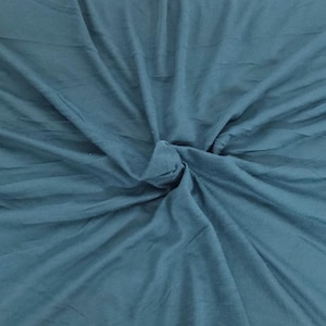 May include: A close-up shot of a teal fabric with a soft, flowing texture. The fabric is gathered and knotted in the center, creating a focal point. The material has subtle variations in tone, adding depth to the overall appearance. The fabric appears to be lightweight and suitable for clothing or crafts.