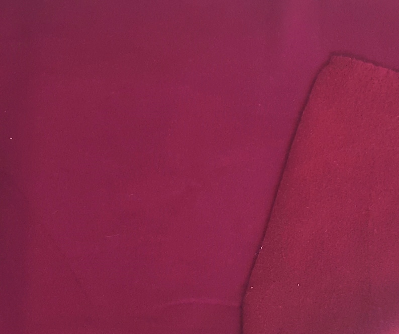 May include: A close-up of a piece of fabric in a deep burgundy color. The fabric has a smooth, matte finish. A smaller, textured piece of the same color fabric is placed diagonally across the corner of the larger piece.