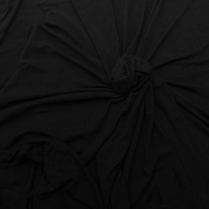 May include: Black fabric with a smooth, soft texture. The fabric is draped and folded, creating a variety of folds and creases.