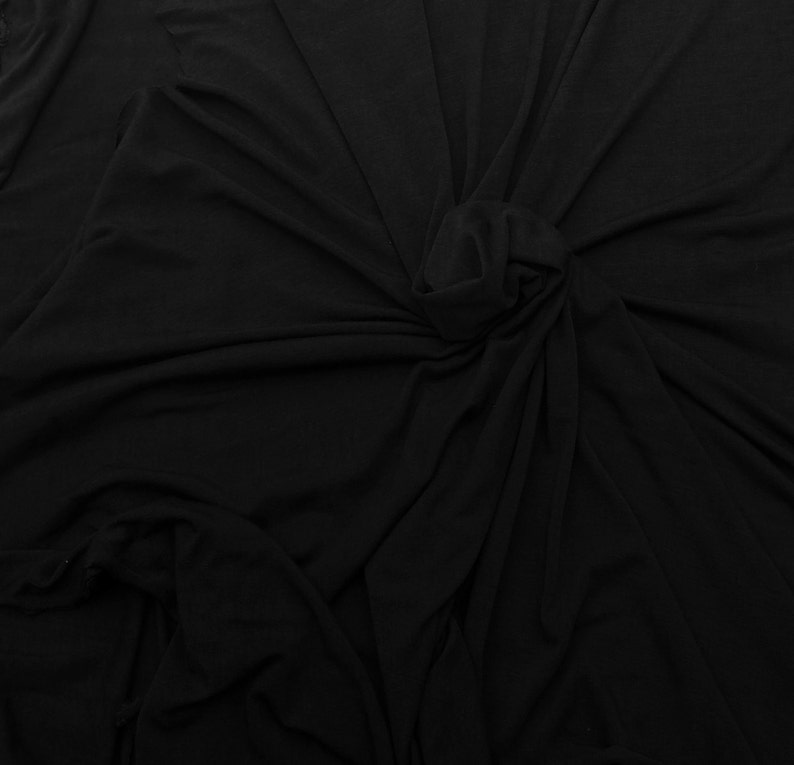 May include: Black fabric with a smooth, soft texture. The fabric is draped and folded, creating a variety of folds and creases.
