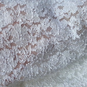 May include: White lace fabric with a delicate floral pattern. The lace is soft and flowing, with a subtle sheen.