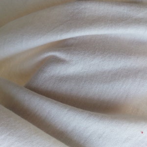 May include: Close-up of a white fabric with a smooth texture. The fabric is folded and has a slight sheen.