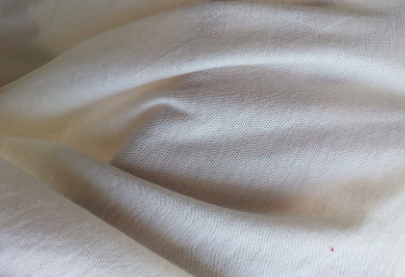 May include: Close-up of a white fabric with a smooth texture. The fabric is folded and has a slight sheen.