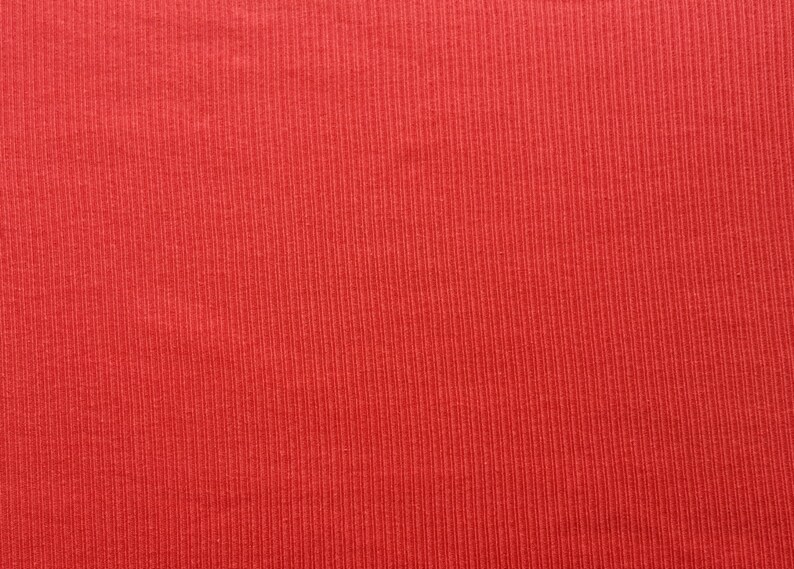 May include: Close-up of a textured, red fabric with vertical ribbing. The material has a consistent color and pattern, suggesting a knit or ribbed textile. The image highlights the fabric's texture and color.
