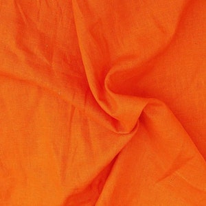 Op de afbeelding: Een close-up van een feloranje stof met een textuur die lijkt op linnen. De stof is gevouwen en gedrapeerd, waardoor zachte plooien en kreukels ontstaan.