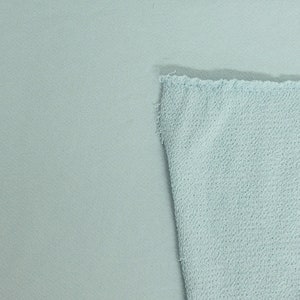 May include: A close-up of two sections of light blue fabric. One section is smooth, while the other has a textured, looped surface. The edges of the textured fabric are frayed, revealing the raw cut.