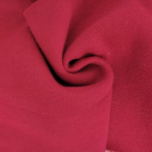 May include: A deep magenta fabric with a soft, matte texture. The material is folded in the center, creating organic curves and shadows that highlight the consistent, solid color and the fine, uniform weave of the textile surface throughout the frame.