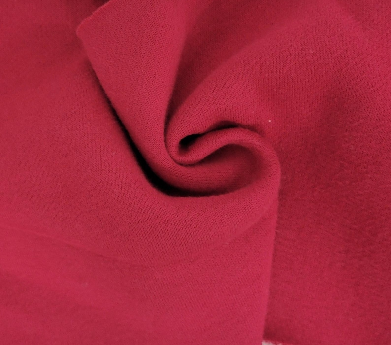 May include: A deep magenta fabric with a soft, matte texture. The material is folded in the center, creating organic curves and shadows that highlight the consistent, solid color and the fine, uniform weave of the textile surface throughout the frame.