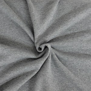 May include: A close-up shot of gray fabric, tightly swirled to create a spiral effect. The fabric has a soft, textured appearance, with subtle variations in tone. The material appears to be a knit or jersey type, suitable for clothing or home textiles.