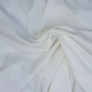 May include: White fabric with a smooth, soft texture. The fabric is folded and draped, creating a flowing, elegant look.