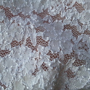 May include: White lace fabric with a delicate floral pattern. The lace is soft and flowing, with a slightly textured surface.