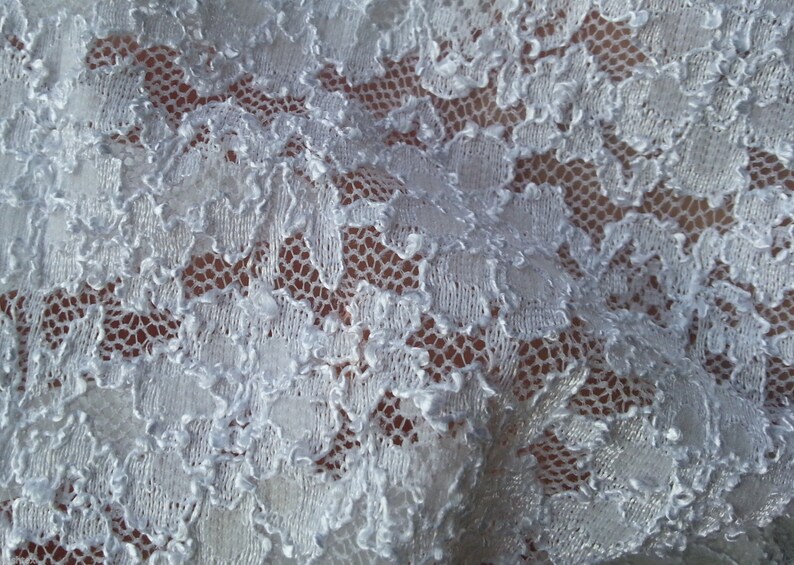 May include: White lace fabric with a delicate floral pattern. The lace is soft and flowing, with a slightly textured surface.