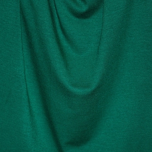 May include: Close-up of a textured, emerald green fabric. The fabric has subtle variations in tone, creating a sense of depth and highlighting the folds and creases. The overall appearance is smooth and rich.