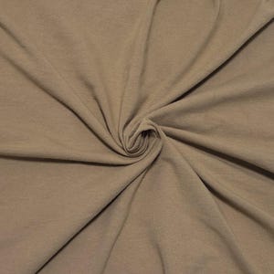 May include: A solid light brown fabric with a soft, matte texture, displayed with a central swirl that creates natural folds and drapes across the surface, highlighting the consistent, neutral earth-toned color throughout the material.