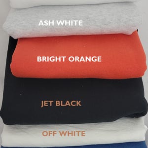May include: A stack of folded fabric in various colors, including bright white, ash white, bright orange, jet black, off white, and ocean blue. Each layer is labeled with its respective color name in a bold font.