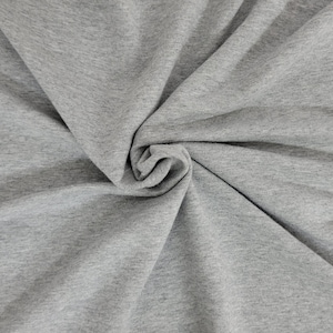 May include: A close-up shot of a gray fabric with a soft, textured appearance. The material is draped and swirled, creating a pattern of folds and shadows. The fabric appears to be a knit or jersey material, suitable for clothing.