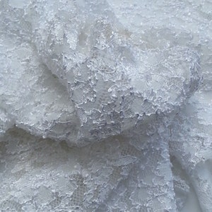 May include: White lace fabric with a delicate floral pattern. The fabric is soft and flowing, and it would be perfect for a variety of projects, such as wedding dresses, tablecloths, and curtains.