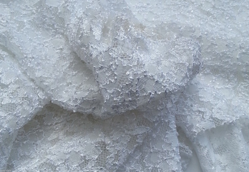 May include: White lace fabric with a delicate floral pattern. The fabric is soft and flowing, and it would be perfect for a variety of projects, such as wedding dresses, tablecloths, and curtains.