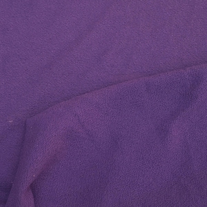 May include: A close-up of a purple fabric with a textured surface. The fabric is folded in half, showing the inside of the fabric.