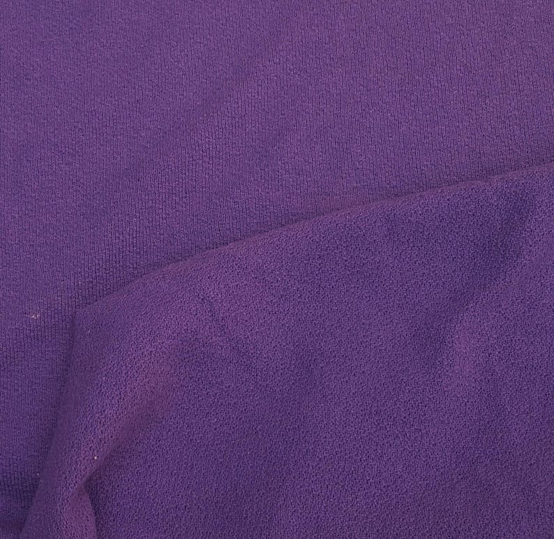 May include: A close-up of a purple fabric with a textured surface. The fabric is folded in half, showing the inside of the fabric.