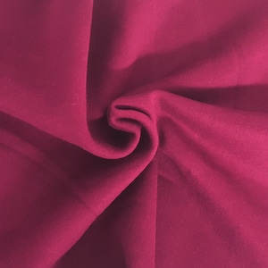 May include: Close-up of a folded piece of fabric in a deep magenta color. The fabric has a soft, velvety texture and is draped in gentle folds, creating shadows and highlights. The overall effect is rich and luxurious.