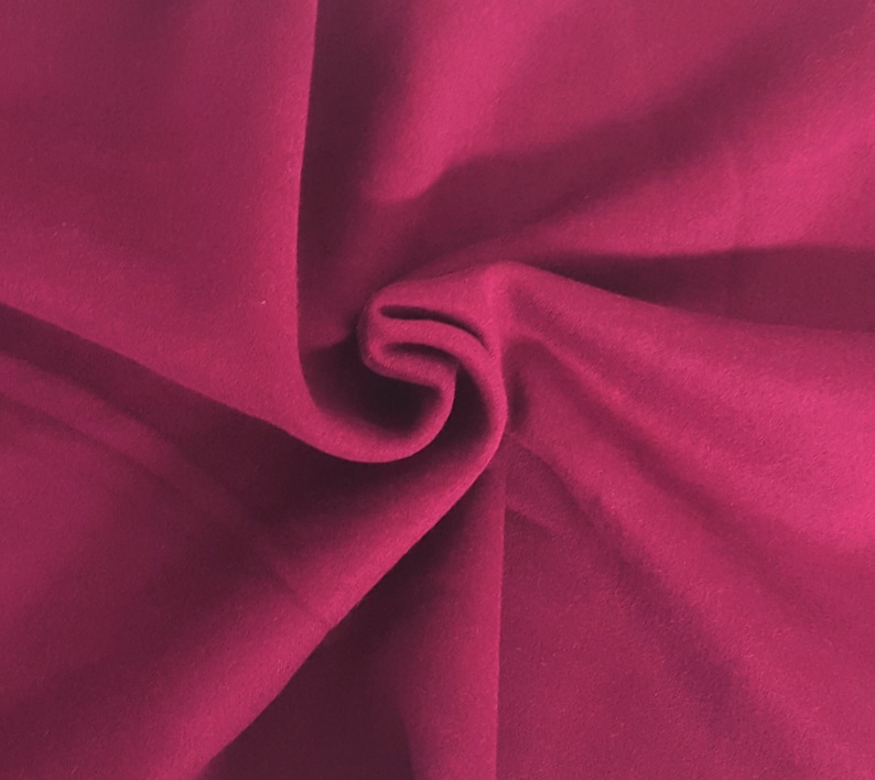 May include: Close-up of a folded piece of fabric in a deep magenta color. The fabric has a soft, velvety texture and is draped in gentle folds, creating shadows and highlights. The overall effect is rich and luxurious.