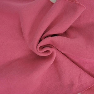 May include: A solid, deep rose-pink fabric with a soft, matte, and slightly fuzzy texture. The material is draped in a central swirl, creating natural folds and shadows that highlight the consistent, uniform color and smooth surface of the textile.