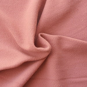 May include: Close-up of a soft, pink fabric with a textured surface. The fabric is folded and draped, showing its texture and drape.