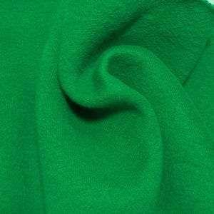 May include: A vibrant, solid green fabric with a soft, slightly fuzzy texture. The material is draped to create gentle folds and curves, highlighting the consistent, saturated emerald green color across the entire surface of the textile.