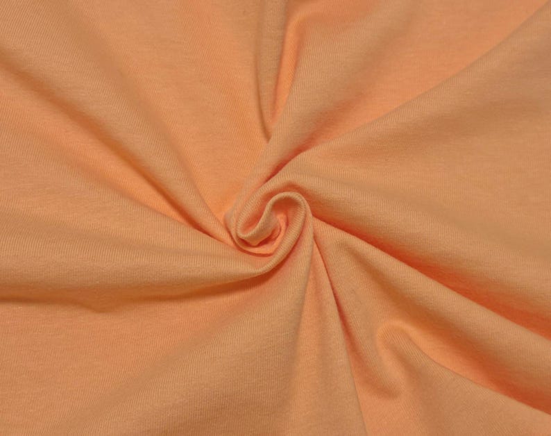 Puede incluir: Una tela de color melocot&oacute;n claro s&oacute;lido con una textura suave y mate. El material est&aacute; recogido en el centro, creando pliegues suaves y radiantes y sombras profundas que resaltan el tono uniforme y consistente en toda la superficie.