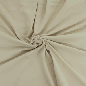 Puede incluir: Una tela de color beige claro s&oacute;lido con una textura suave, mostrada con un punto central fruncido que crea pliegues radiantes y sombras suaves en toda la superficie, resaltando el color consistente y el acabado mate del material.