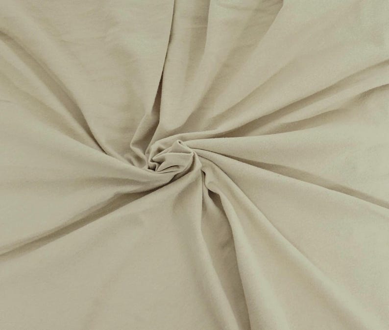 Puede incluir: Una tela de color beige claro s&oacute;lido con una textura suave, mostrada con un punto central fruncido que crea pliegues radiantes y sombras suaves en toda la superficie, resaltando el color consistente y el acabado mate del material.