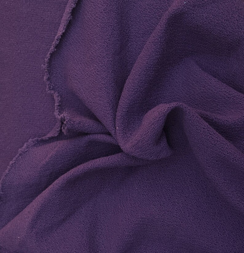 May include: Close-up of a deep purple fabric with a textured surface. The fabric is folded and draped, showing its soft and drapey texture.