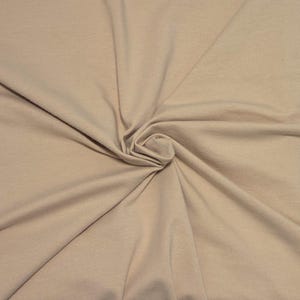 May include: A solid light beige fabric with a smooth, matte texture. The material is gathered in the center, creating soft, radiating folds and natural drapes that extend outward across the entire surface, showcasing the consistent neutral color.