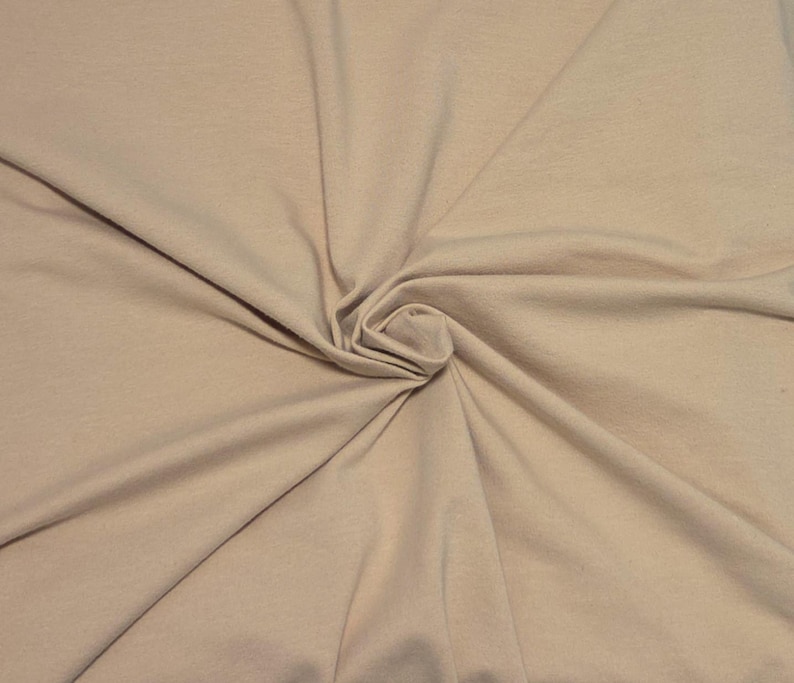 May include: A solid light beige fabric with a smooth, matte texture. The material is gathered in the center, creating soft, radiating folds and natural drapes that extend outward across the entire surface, showcasing the consistent neutral color.
