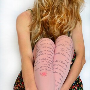 Puede incluir: Una mujer lleva un vestido rosa con estampado floral y medias rosas con un extracto impreso de Alicia en el País de las Maravillas. El texto en las medias dice "...waving the...must be, said the...Cat, or you...wouldn't have come...didn't think that...she went on...how do you...know..."