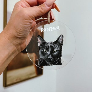 May include: A clear round bauble with a black cat painted on it. The cat's name, "Panzer", is written in white lettering at the top of the bauble.
