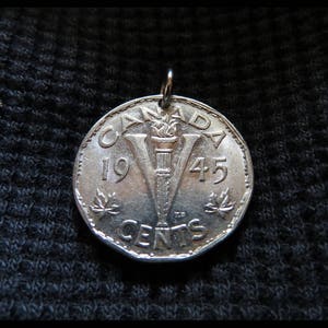Op de afbeelding: Een zilveren hanger gemaakt van een Canadese munt. De munt toont het woord "CANADA", het jaar "1945" en een "V" met een fakkel. De hanger heeft een kleine lus aan de bovenkant voor een ketting.