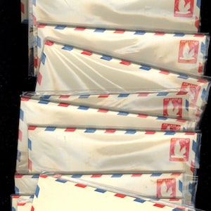 May include: A stack of vintage airmail envelopes in clear plastic packaging. The envelopes are white with red and blue diagonal stripes along the edges. Each envelope has a red stamp with a white bird and the text "AIR MAIL 6¢ POSTAGE".