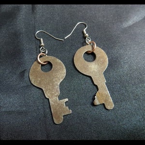 May include: A pair of handmade earrings featuring vintage key charms. The earrings have silver-colored ear wires and copper-colored jump rings. The key charms are a rusty brown color and have a keyhole shape.