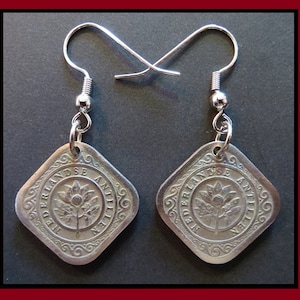Puede incluir: Un par de pendientes colgantes de tono plateado con monedas cuadradas de las Nederlandse Antillen. Cada moneda muestra un motivo floral central rodeado de texto y un borde decorativo, suspendidas de ganchos de metal de tono plateado.