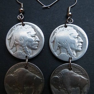 May include: A pair of silver-toned earrings. Each earring features a coin with a profile of a Native American on the top and a buffalo on the bottom. The earrings are suspended from silver-colored ear wires.