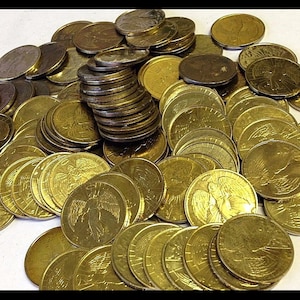 May include: A collection of gold-colored coins, some stacked and others scattered. The coins feature detailed relief designs, including an eagle and a figure. The coins have a shiny, metallic appearance.