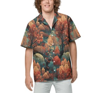 May include: Short-sleeved button-down shirt with a vibrant forest print in shades of orange, red, green, and yellow. The shirt is paired with light gray shorts. The overall style is casual and relaxed.