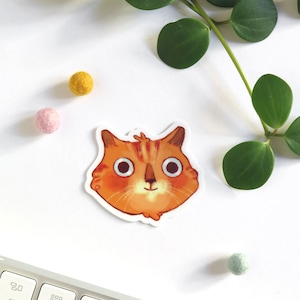 Autocollant avec une illustration d'une tête de chat roux qui sourit