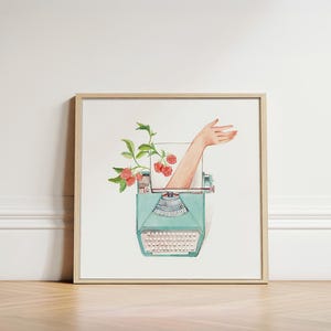 Puede incluir: Impresión artística en acuarela enmarcada. La obra presenta una máquina de escribir turquesa vintage con una mano que emerge, acompañada de frambuesas y hojas verdes. La impresión se exhibe sobre un suelo de madera.