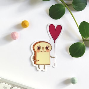 Sticker with an illustration of a cute toast holding a red heart shaped balloon